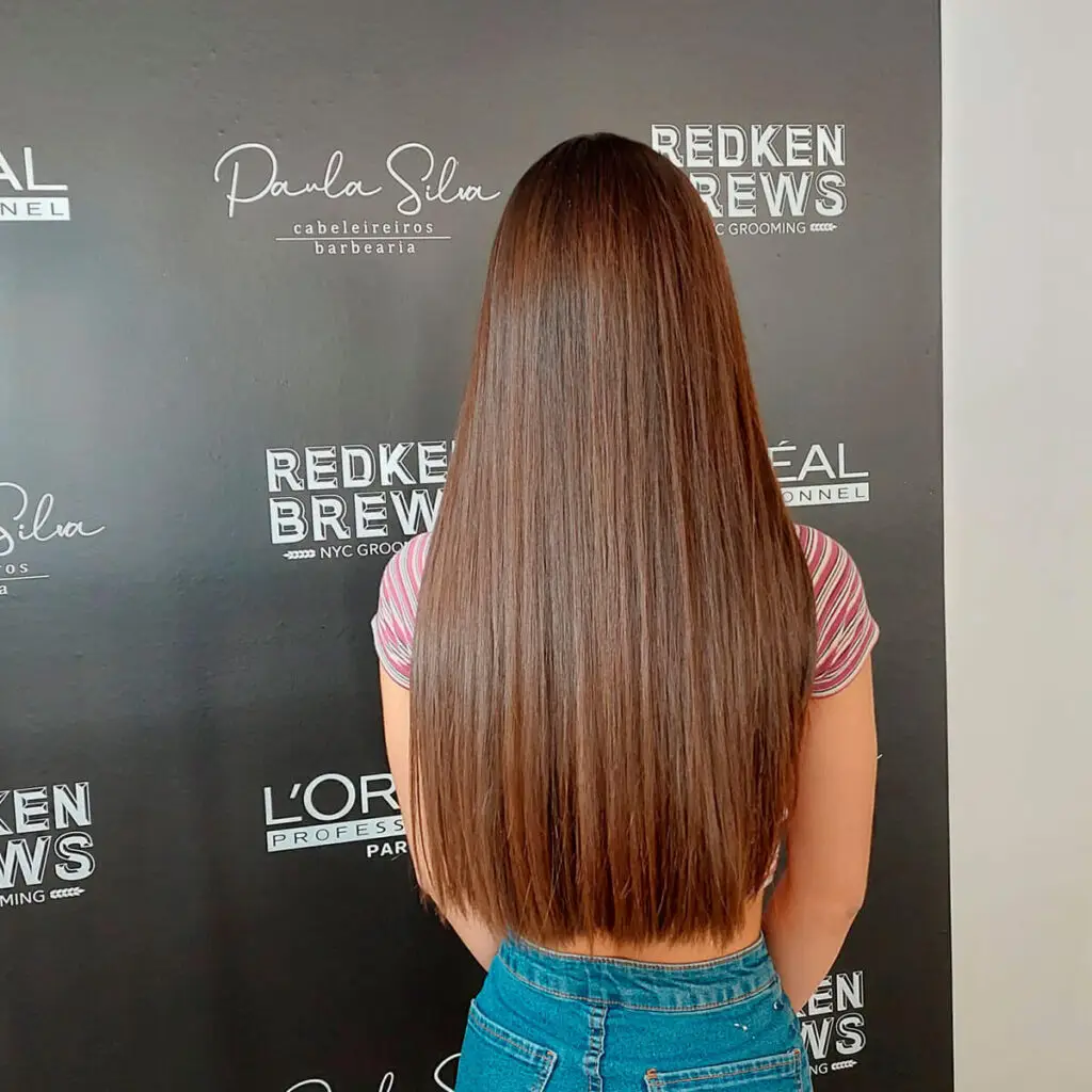 Cabelo comprido liso com coloração castanha brilhante e acabamento alinhado, resultado de tratamento e styling profissional.