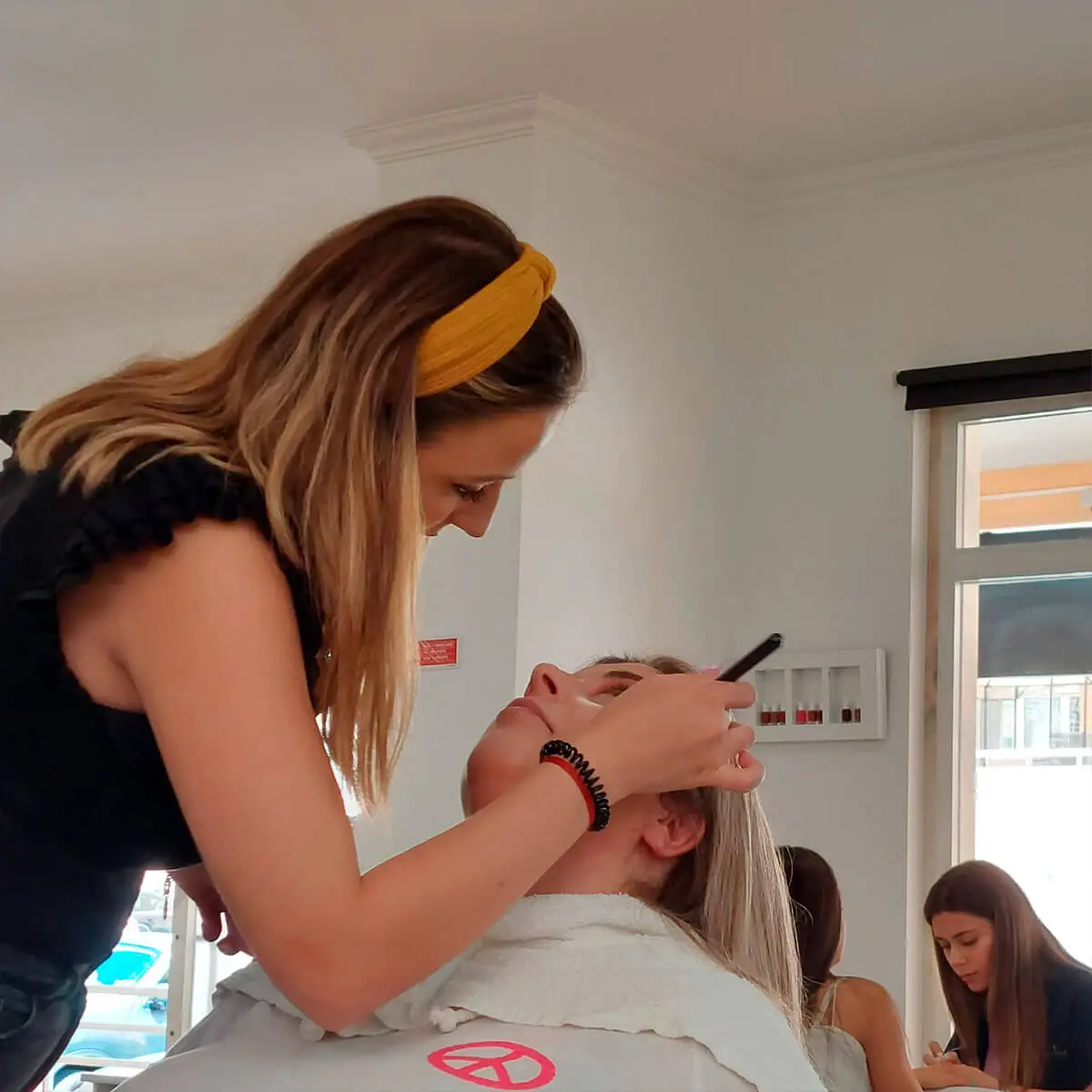 Profissional do salão Paula Silva Cabeleireiros aplicando maquilhagem em cliente, com um ambiente claro e organizado ao fundo.